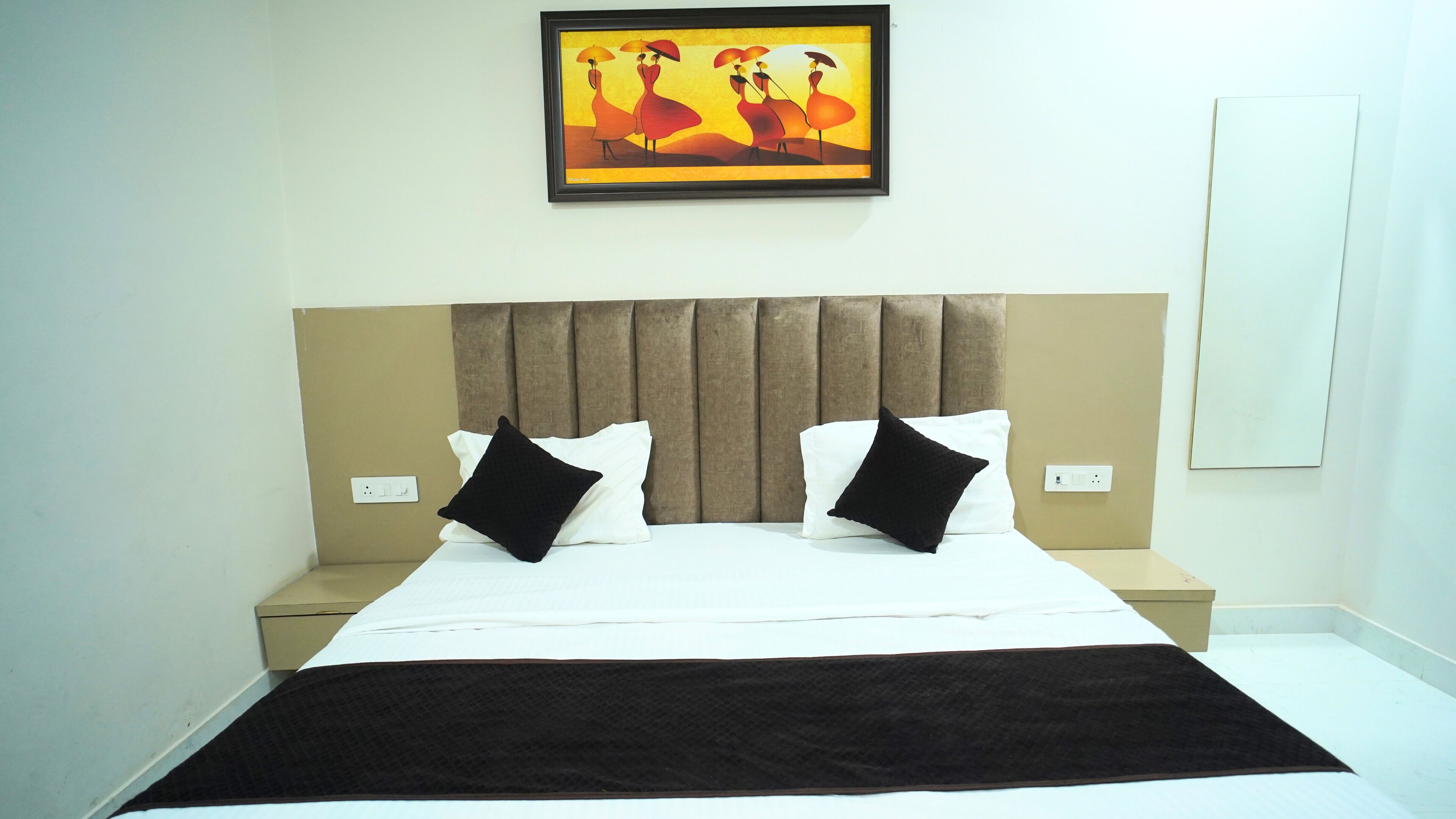A hotel room with a large bed, two bedside tables, a headboard, and a framed artwork on the wall.