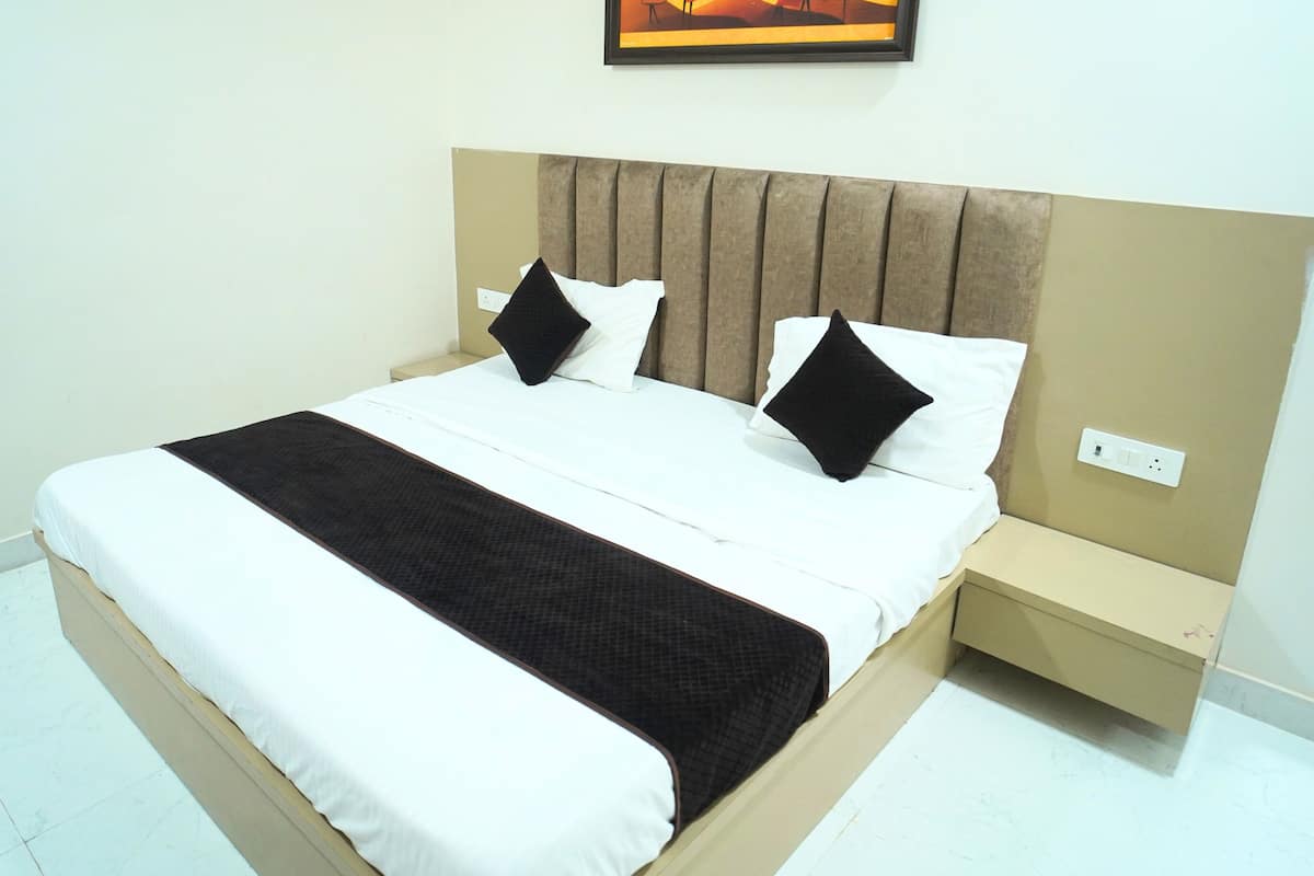 A neatly made bed with white and black bedding, a headboard with vertical slats, and a single nightstand with a power outlet.