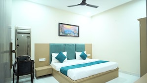 A bedroom with a bed, a chair, a nightstand, a painting, and a ceiling fan. - Hotel Shri Radha Sneh Mathura (Mathura)