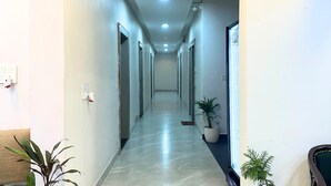 A long, narrow hallway with doors on both sides, a tiled floor, and potted plants along the right wall. - Hotel Shri Radha Sneh Mathura (Mathura)