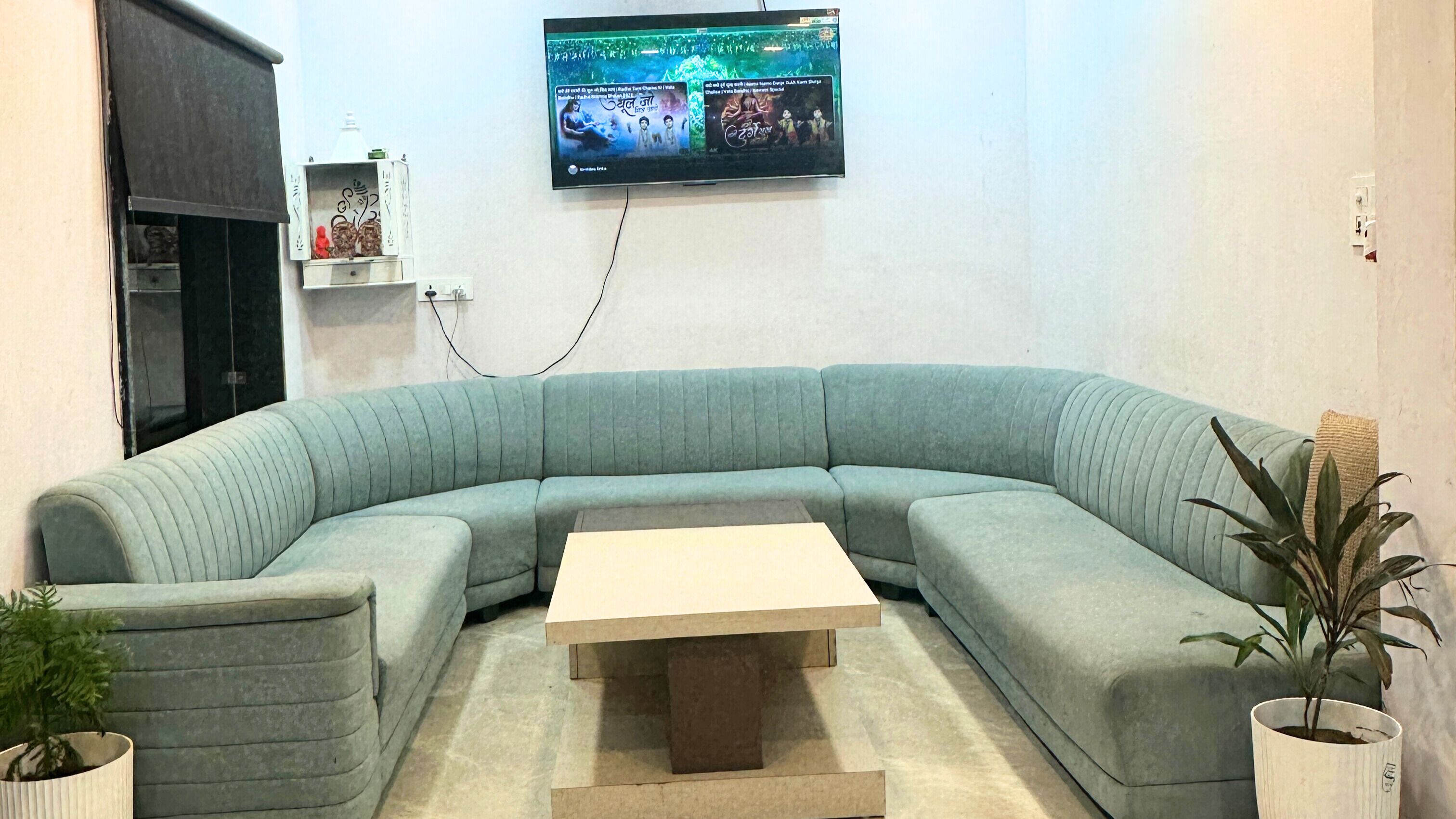 A modern living room with a curved sectional sofa, a central coffee table, and a flat-screen TV mounted on the wall.