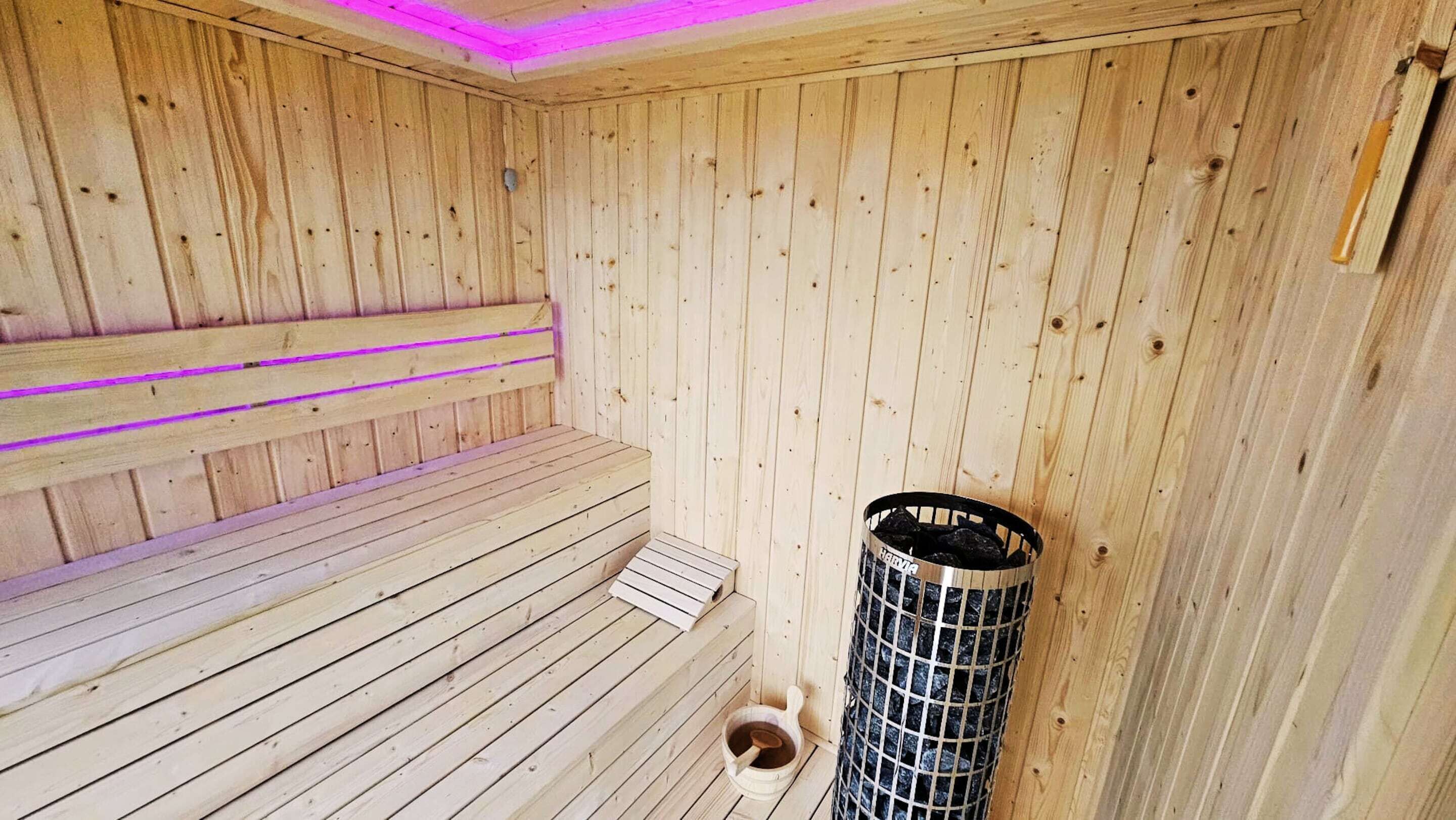 Eine Holzsauna mit Bänken, einem Metallbehälter und einem Holzeimer.