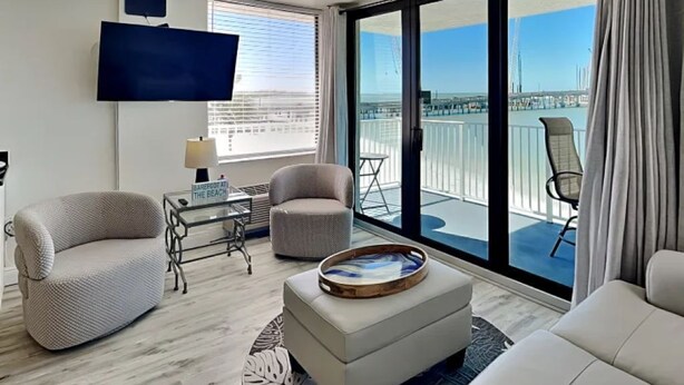 Ein modernes Wohnzimmer mit Fernseher, zwei Sesseln, einer Couch und einem Balkon mit Blick auf die Stadt.