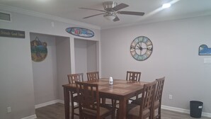 A dining room with a wooden table and chairs, a clock, and a ceiling fan.