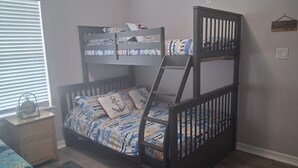 A bunk bed with a patterned bedspread, a nightstand with a lamp, and a window with blinds.