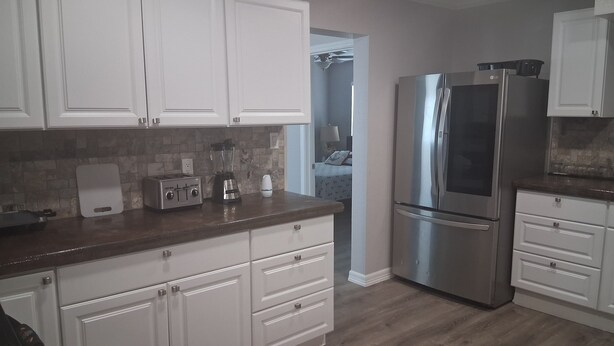 A kitchen with white cabinets, a stainless steel refrigerator, a toaster, and a blender on the counter.