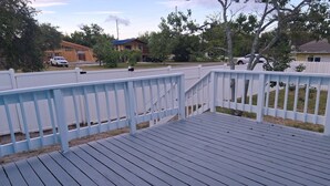A wooden deck with a white railing, surrounded by trees and houses.