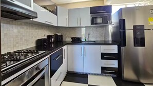 A modern kitchen with white cabinets, a black countertop, a stainless steel refrigerator, and a gas stove. - Your Retreat in Roldanillo! (Roldanillo)