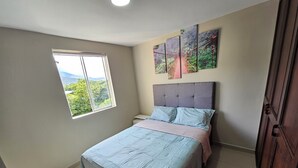 A bedroom with a bed, a window with a view of greenery, and a door. - Your Retreat in Roldanillo! (Roldanillo)