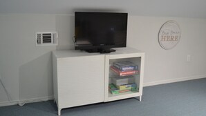 A white entertainment unit with a flat-screen TV and a shelf with board games. - Charming studio in peaceful Long Beach with AC (Long Beach)