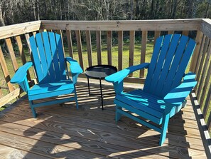 Um deck de madeira com duas cadeiras Adirondack azuis e uma pequena mesa redonda.