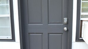 A dark gray door with a keypad lock, a doormat with a floral pattern, and a window with a white frame to the left. - Charming studio in peaceful Long Beach with AC (Long Beach)