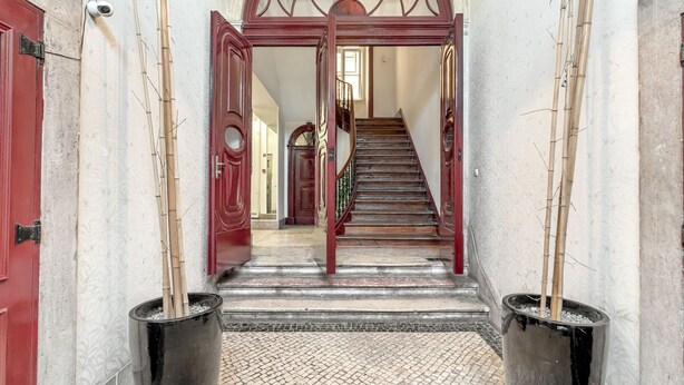 A grand staircase with a red handrail and a patterned floor leading to a door with a decorative arch.