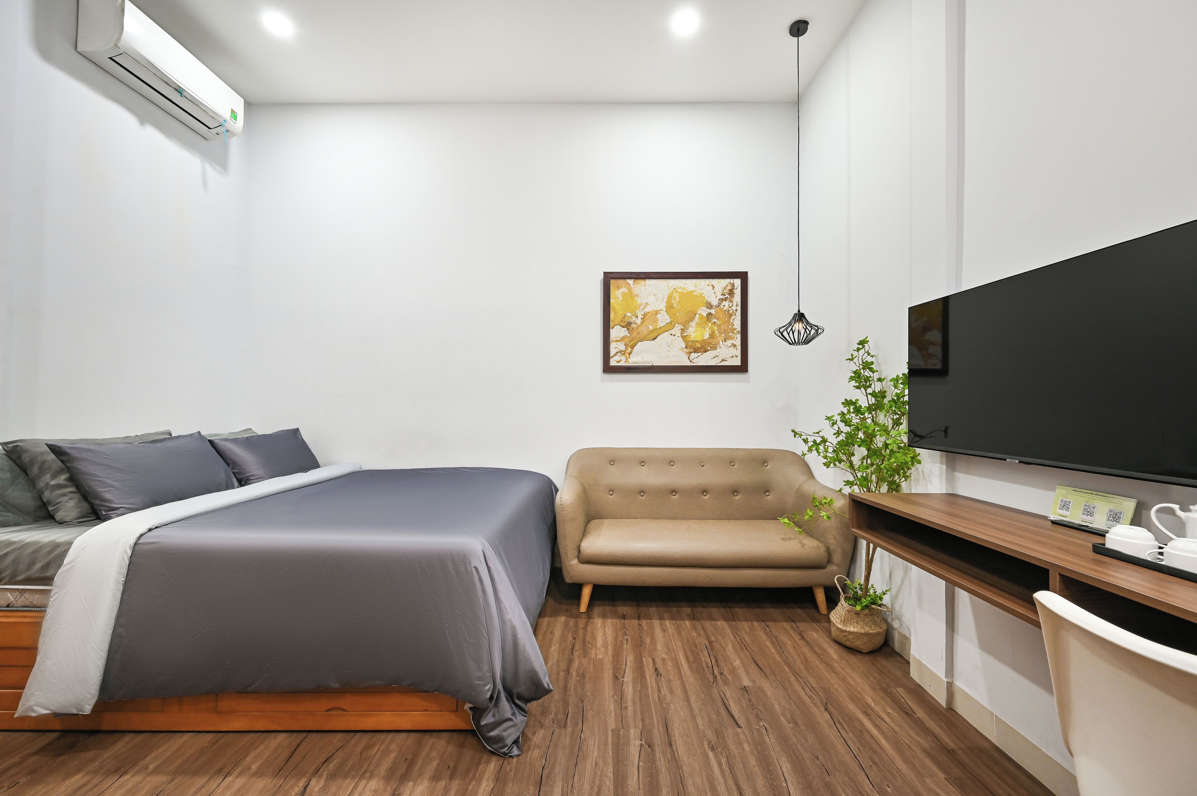 Ein Schlafzimmer mit einem Bett, einem Sofa, einem Fernseher und einem Schreibtisch mit einer Pflanze.