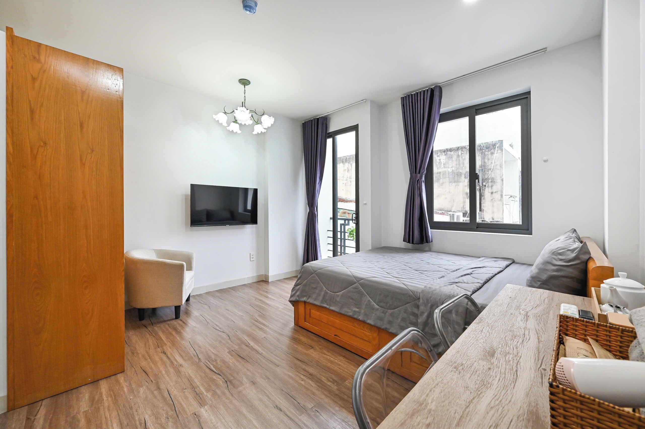 Ein Schlafzimmer mit einem Bett, einem Fernseher, einer Holztür, einem Sessel, einem Tisch und einem Fenster.