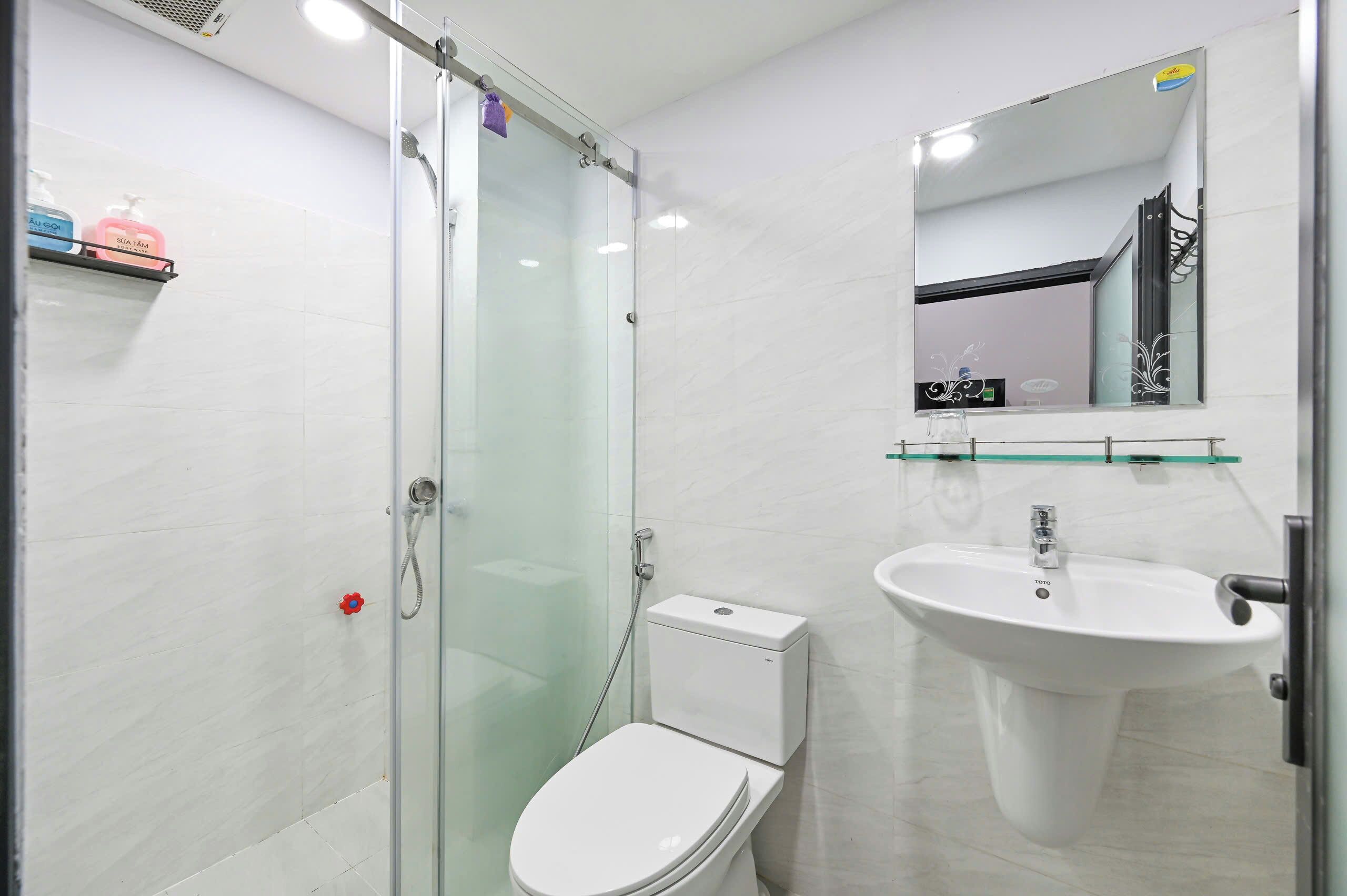 Een moderne badkamer met een glazen douchecabine, een wit toilet en een wastafel op voet.