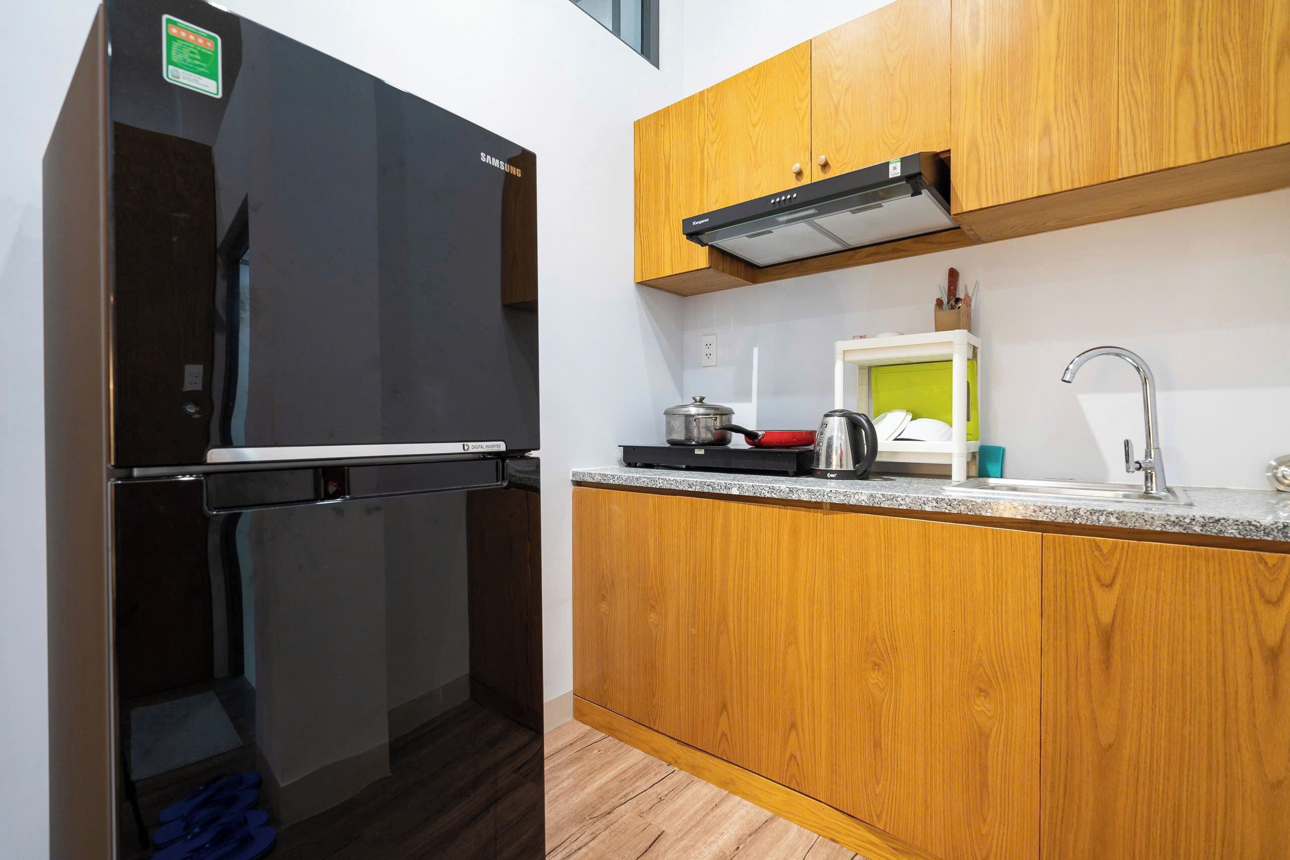 A compact kitchen with a black refrigerator, wooden cabinets, a stainless steel sink, and a microwave.