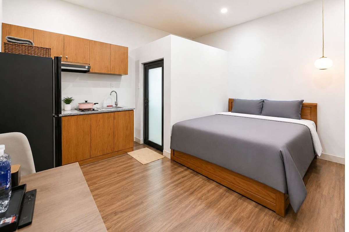 Ein kleines Hotelzimmer mit Küchenzeile, einem Bett, Holzboden und einer Deckenleuchte.