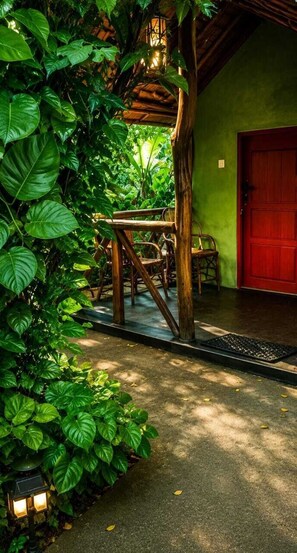 A covered outdoor seating area with a table and chairs, surrounded by lush greenery and a red door. - Furahia Eco Inn (Arusha)