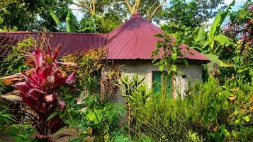 Un pequeño edificio con techo rojo rodeado de abundante vegetación y diversas plantas.