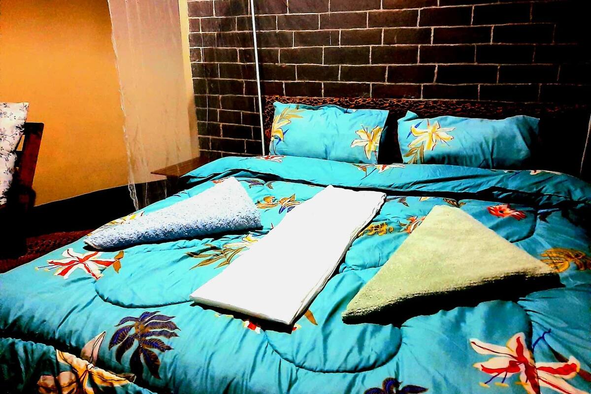 Una cama con edredón estampado, almohadas y una manta.