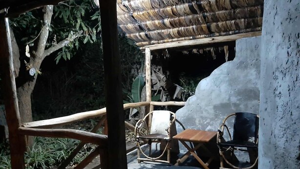 A wooden deck with a thatched roof, a rustic chair, and a large ice sculpture. - Furahia Eco Inn (Arusha)