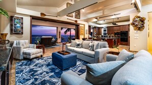 Un salón amplio con un ventanal grande con vistas al océano, una cocina con alacenas de madera oscura y un comedor con barra.