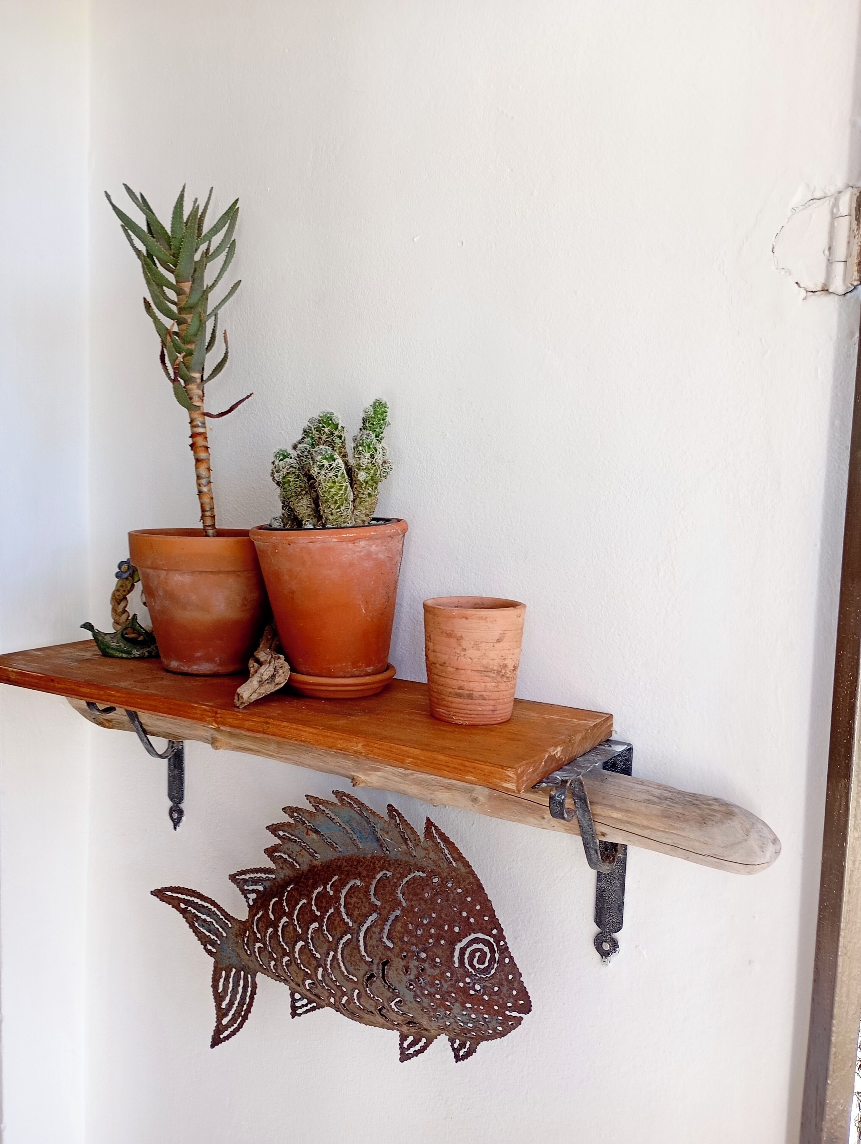 Una estantería de madera con macetas de terracota con plantas, una cajita de madera y un adorno de pez de metal.