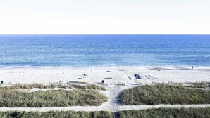 A beach with a clear path leading to the water, surrounded by dunes and sparse vegetation. - Parrot-ise by StayMareni - Oceanfront Suite (Myrtle Beach)