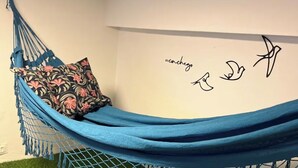 A hammock bed with a floral pillow, a wall with a simple design, and artificial grass. - Charming loft in BH (Nova Esperança Belo Horizonte)