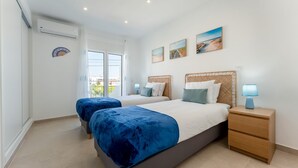 A bedroom with two beds, a nightstand, and a window with a view.