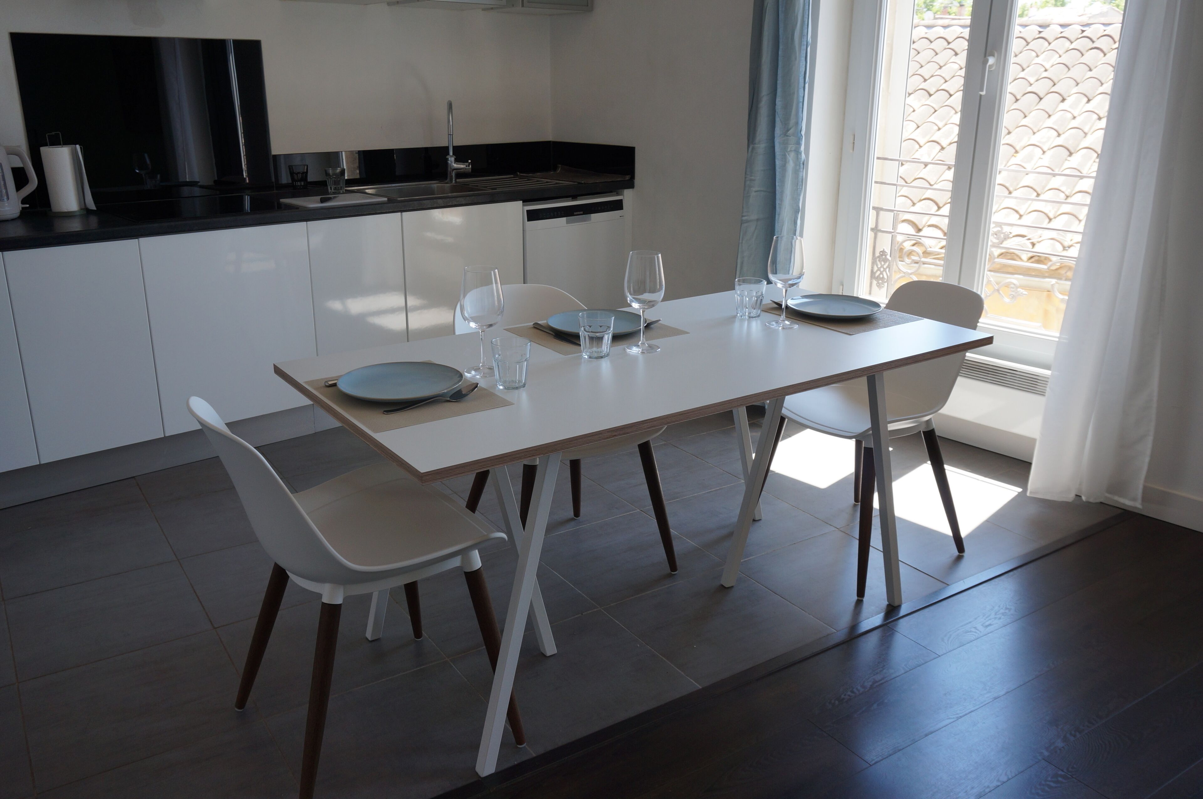 Cocina moderna con una mesa de comedor preparada para cuatro personas, sillas blancas y vistas al exterior a través de una puerta corredera.