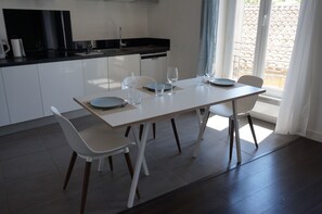 Eine moderne Küche mit Esstisch für vier Personen, weißen Stühlen und Blick nach draußen durch eine Schiebetür.