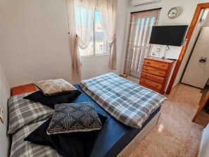 Une chambre à coucher avec un lit, une commode en bois, un téléviseur et une fenêtre avec des rideaux.