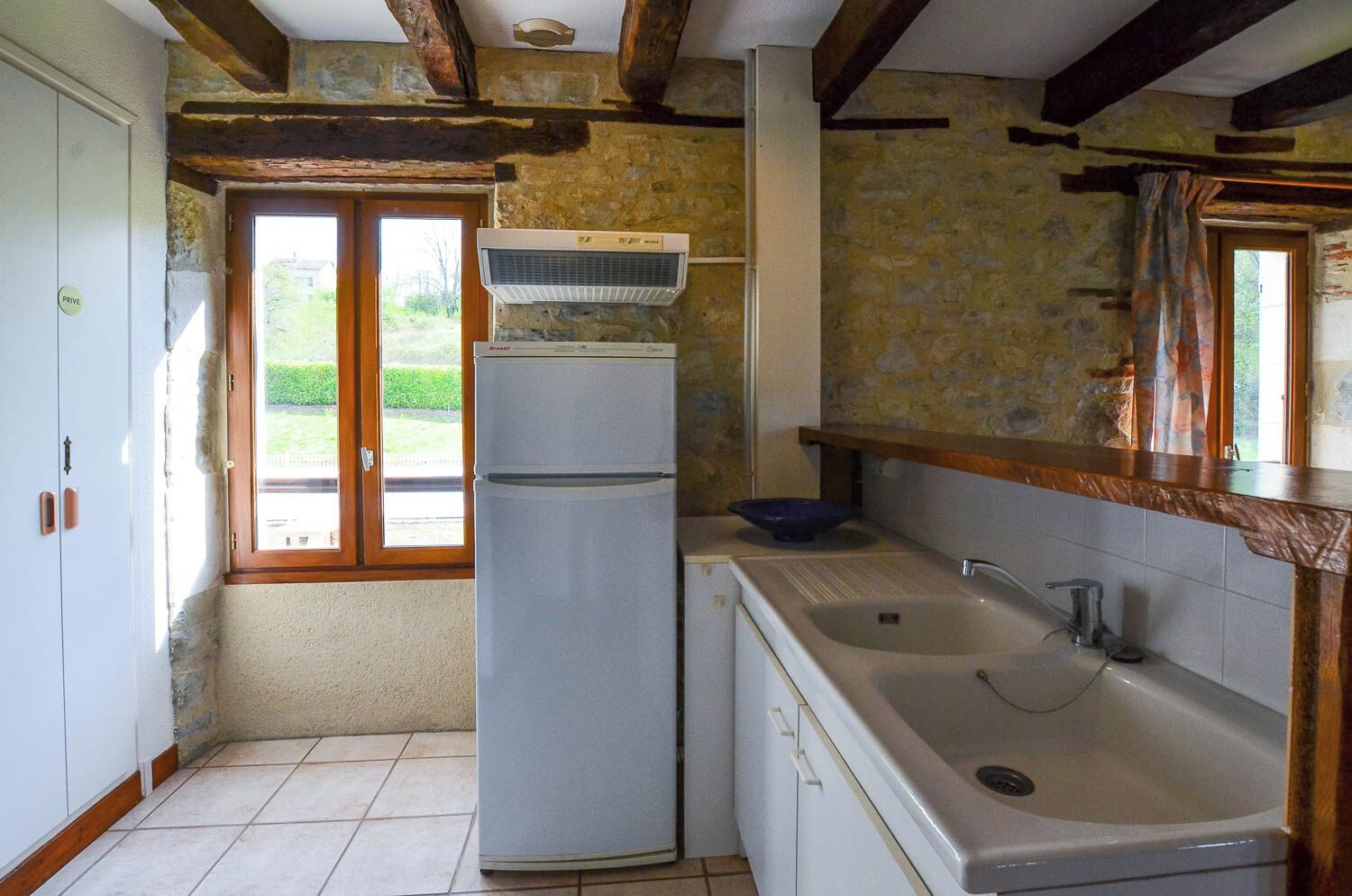 Eine kompakte Küche mit integriertem Kühlschrank, Spüle und Fenster mit Blick auf Grünflächen.