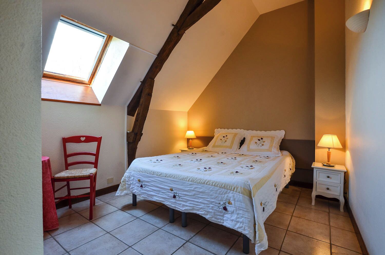 A bedroom with a sloped ceiling, a bed with floral bedding, a red chair, and two bedside lamps.