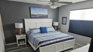 A bedroom with a bed, nightstands, a ceiling fan, a window with blinds, and artwork on the walls. - Charming 2-bedroom house in fabulous The Villages with AC (The Villages)