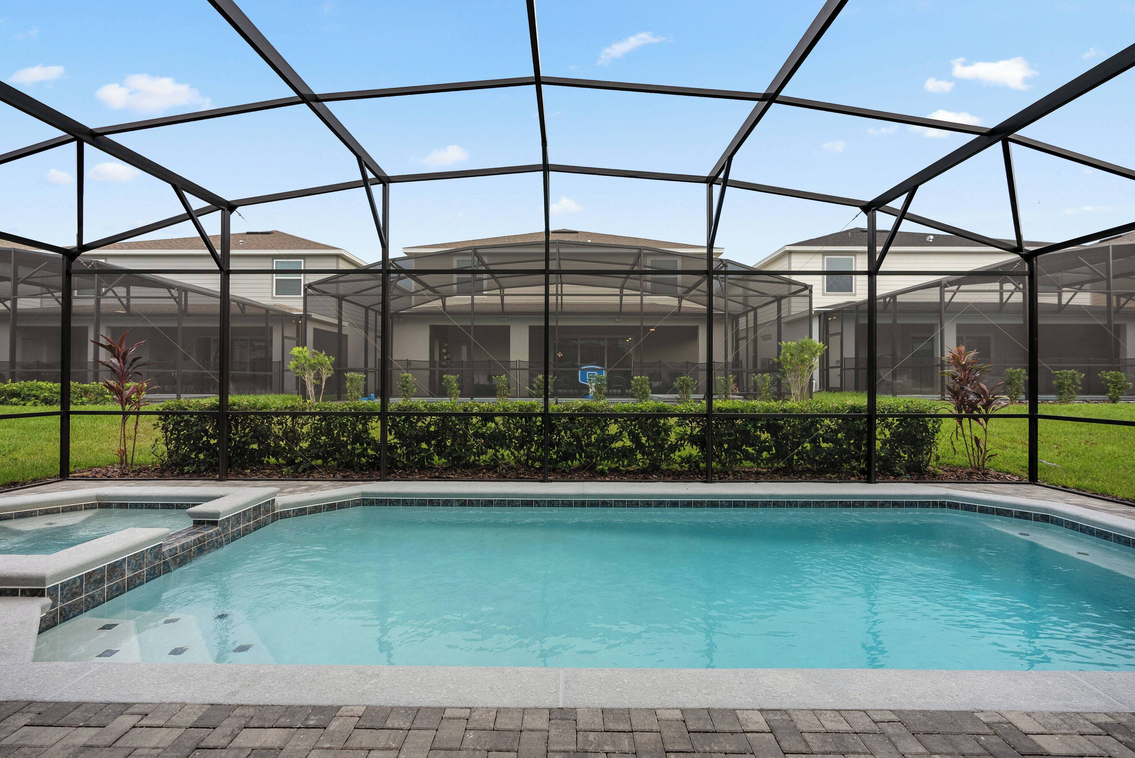 A swimming pool with a glass enclosure, surrounded by a landscaped area and a view of a residential building.