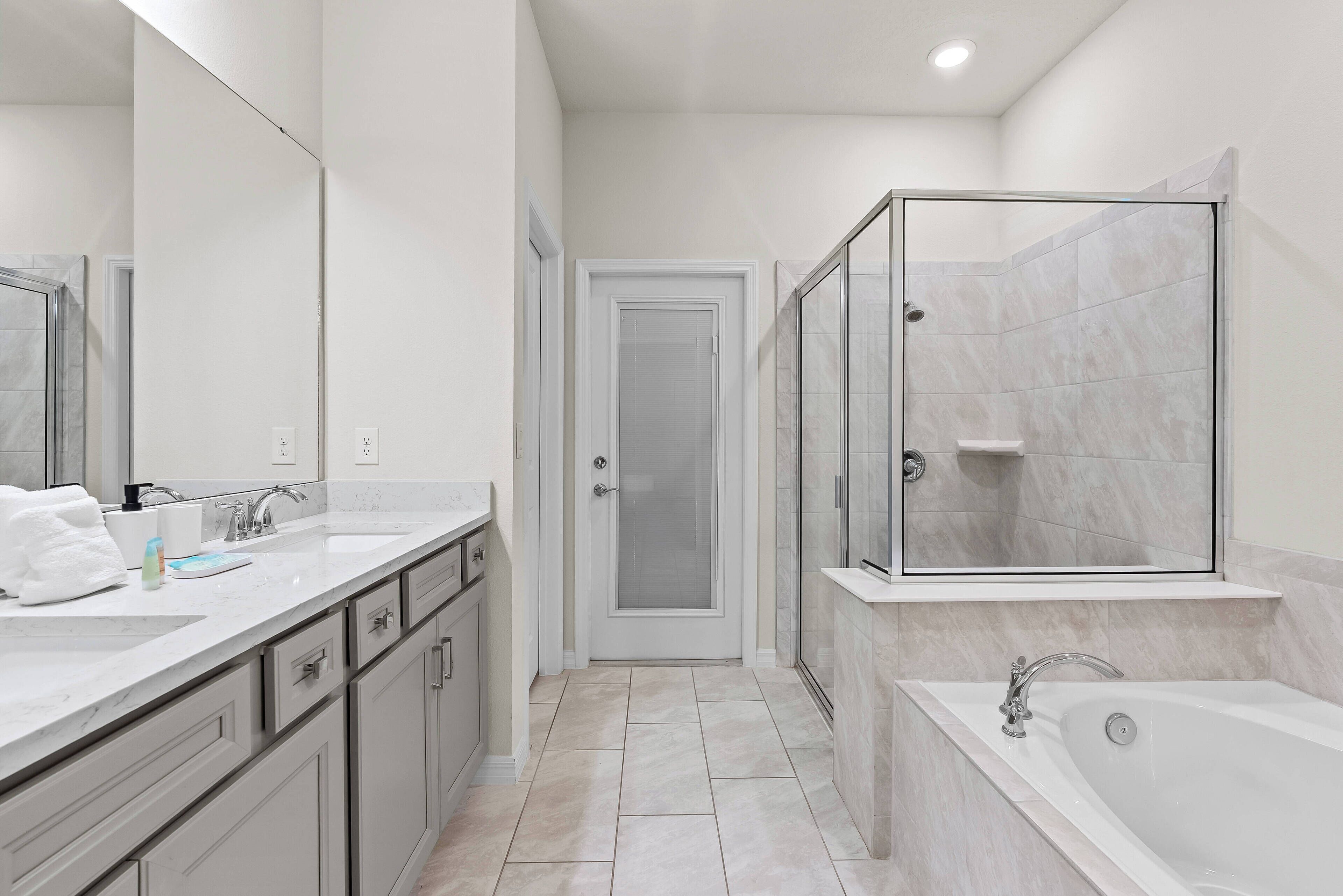 A modern bathroom with a large mirror, a shower enclosure, a bathtub, and a vanity with a sink and countertop.