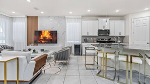 A modern kitchen with white cabinets, a built-in microwave, and a large TV displaying a fire.