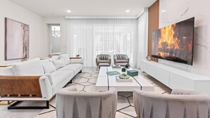 A modern living room with a white sofa, two armchairs, a coffee table, and a TV mounted on the wall.