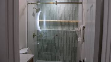 A modern bathroom with a glass-enclosed shower, a toilet, and a sink.