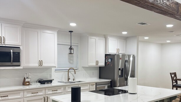 A modern kitchen with white cabinetry, stainless steel appliances, and a central island with bar stools. - Cozy Home in Baton Rouge (Baton Rouge)