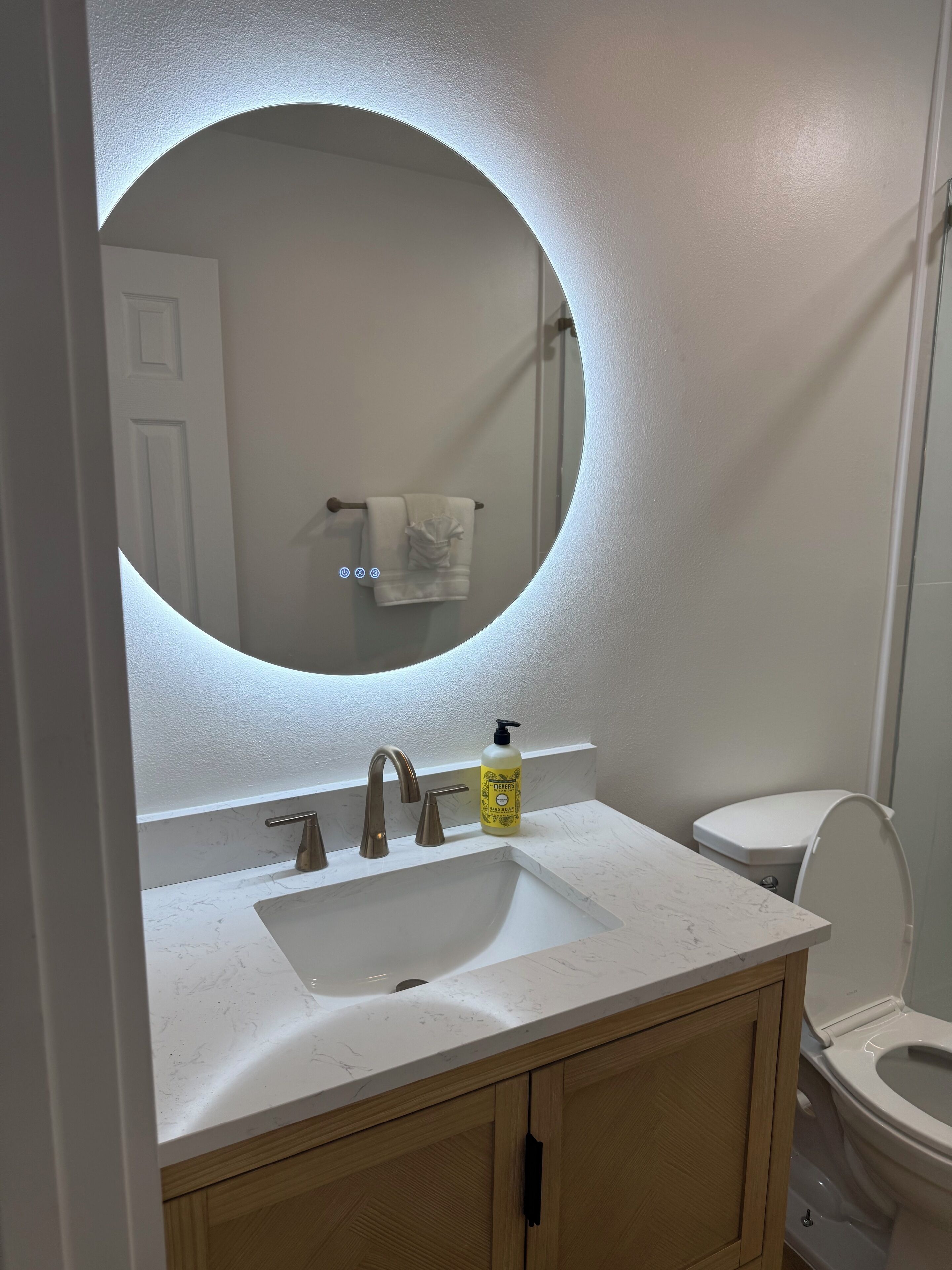 A bathroom with a white sink, a round mirror, and a toilet.