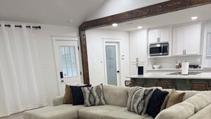 A modern living room with a sectional sofa, wooden flooring, and a kitchen in the background. - Cozy Home in Baton Rouge (Baton Rouge)