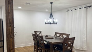 A dining area with a wooden table and chairs, a chandelier, and a white curtain. - Cozy Home in Baton Rouge (Baton Rouge)