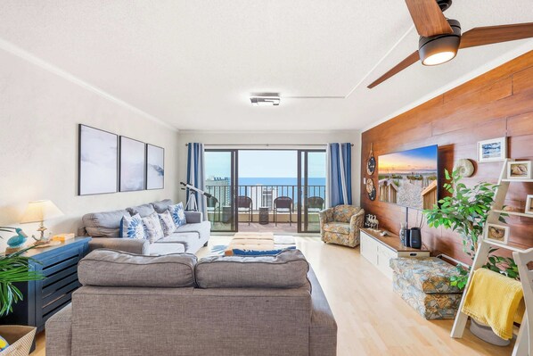 A living room with a sofa, armchairs, a coffee table, a TV, and a balcony with a view. - Top Floor Modern with Ocean View | Pool | Hot Tub (Myrtle Beach)
