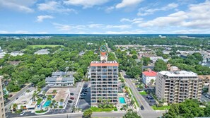 A multi-story hotel with a rooftop pool, surrounded by greenery and other buildings. - Top Floor Modern with Ocean View | Pool | Hot Tub (Myrtle Beach)