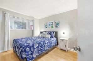 A bedroom with a bed, a bedside table, a nightstand, and a window with blinds. - Top Floor Modern with Ocean View | Pool | Hot Tub (Myrtle Beach)