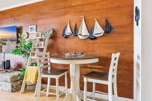 A room with a wooden wall, a round table with white chairs, a TV, and a plant.
